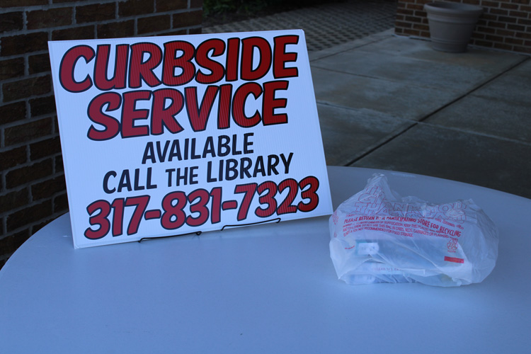 curbside service sign on table with bag of library items