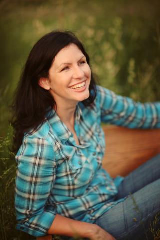 Mindy McGinnis, a white woman with long brown hair. She is wearing a turquoise plaid button up shirt and blue jeans.